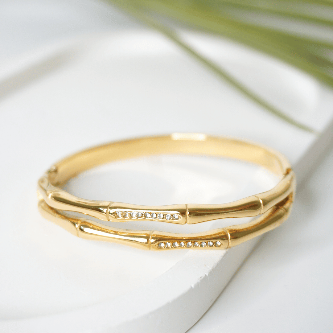 Gold bracelet on a white surface with a blurred green leaf in the background